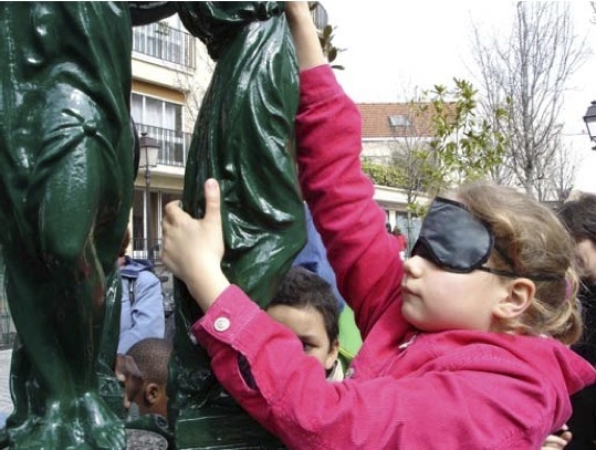 Un enfant avec un bandeau sur les yeux touche une fontaine parisienne
